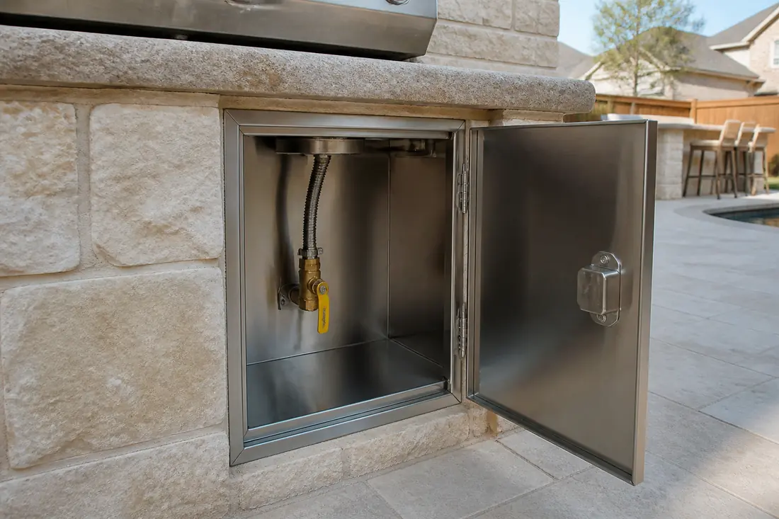 A gas shutoff valve inside a grill island behind an open stainless access door