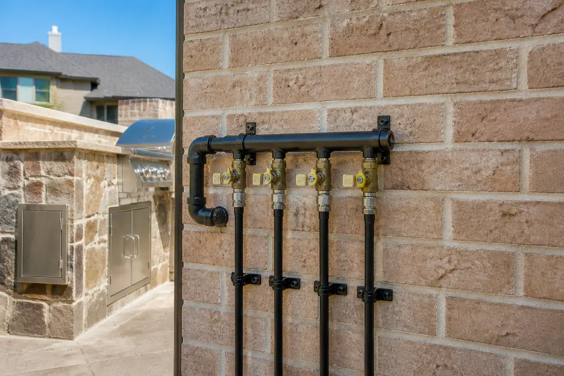 A gas manifold on an exterior house wall with several labeled branch valves