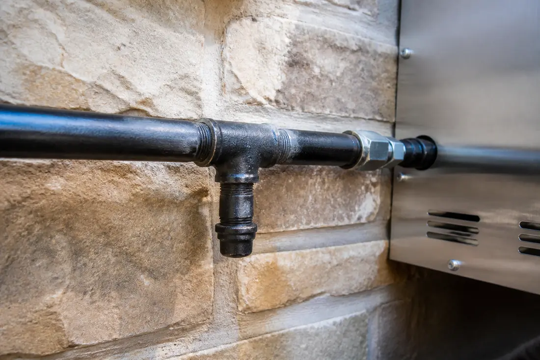 A tee fitting in a black steel gas line with a short capped nipple pointing down