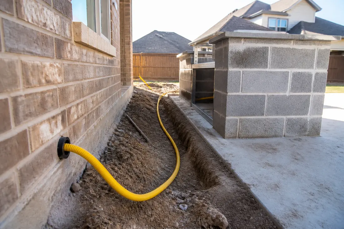 A run of yellow corrugated stainless steel gas tubing leaving a house wall toward a masonry grill island