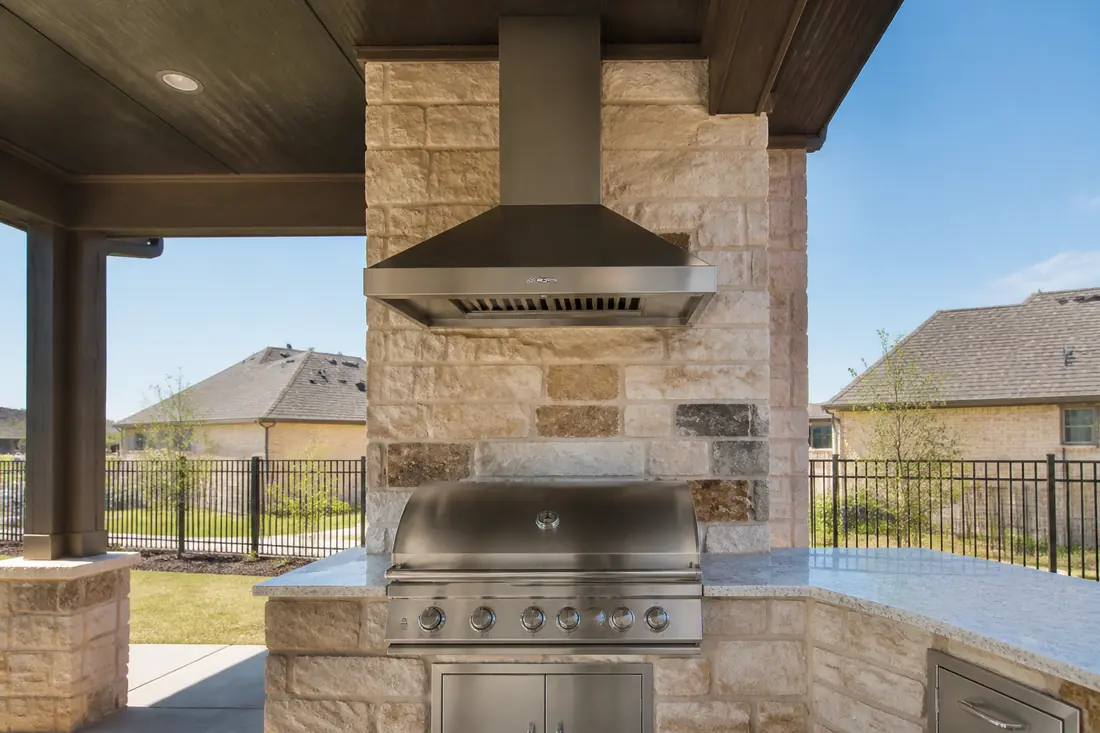 A stainless vent hood mounted above a built-in grill under a patio roof