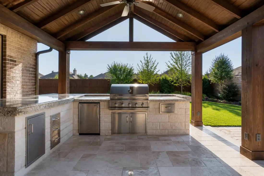 A covered outdoor kitchen with a grill island beneath a solid roof